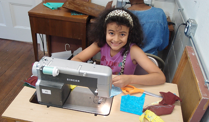 A young girl working at a sewing machine and smiling.