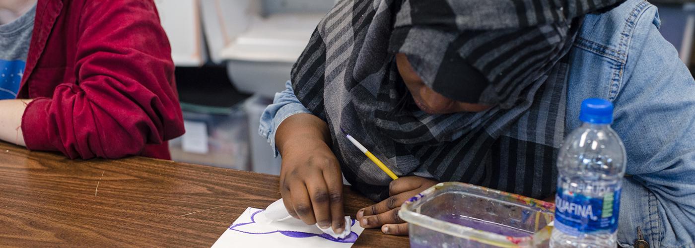 Watercolor Student A young woman in a hijab leans over her artwork as she watercolors